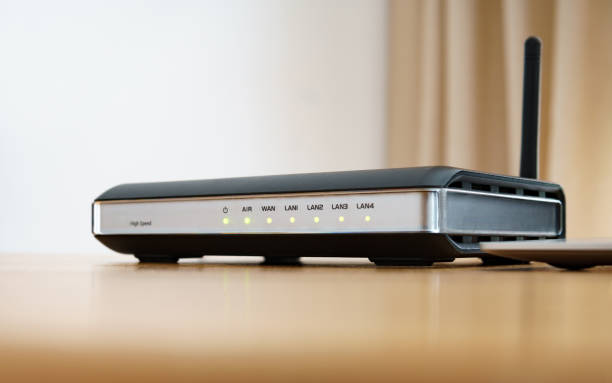 Modern wireless router with indicator lights and external antenna on a wooden desk, illustrating connectivity.